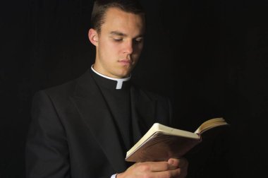 Young Priest, in black, reading Prayer book clipart