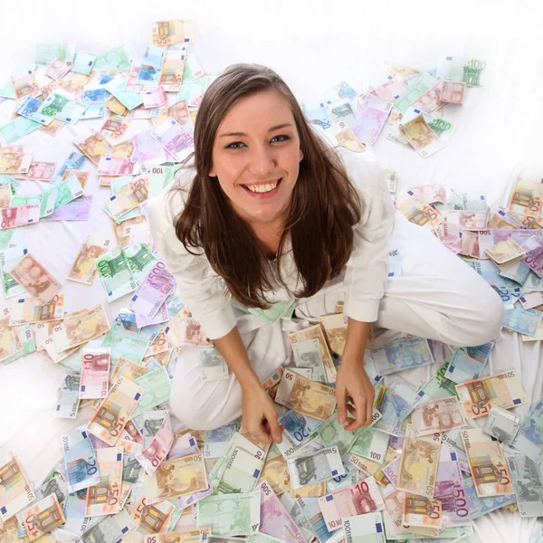 若い女性はお金の中で幸せに座っている 彼女は多くのユーロ紙幣に座っている — ストック写真
