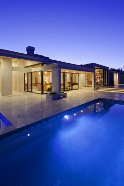 Rear view of luxury villa at night time with swimming pool clipart