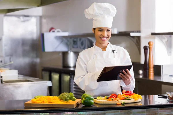 Portrait of a smiling young female chef using digital tablet while cutting vegetables in the kitchen