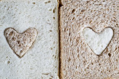 Close up of a white bread slice with a brown wholemeal heart, and a wholemeal bread slice with a white  heart. clipart