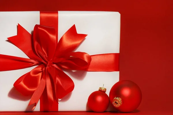 Kırmızı Arka Planı Noel Toplarıyla Büyük Kırmızı Bir Fiyonk Hediye — Stok fotoğraf