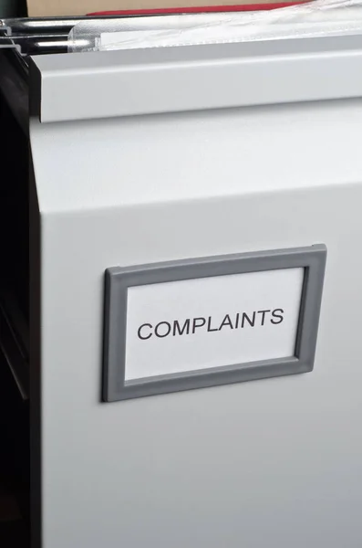 An opened filing cabinet drawer labeled 'Complaints', exposing hanging files and documents within.  Portrait orientation.