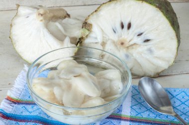 Bowl of white flesh of soursop fruit in front of whole cut fruit on rustic wooden white table clipart