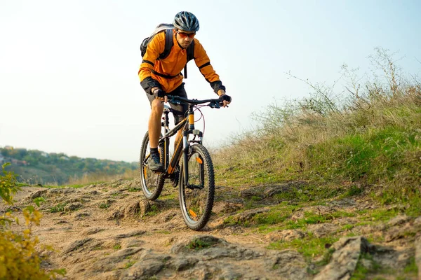 Cyclist in Orange Riding the Mountain Bike on the Autumn Rocky Enduro Trail. Extreme Sport and Enduro Biking Concept.