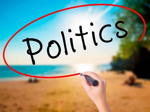 Women Hand writing Politics with black marker on visual screen. Isolated on beach. Business, technology, internet concept. Stock Image