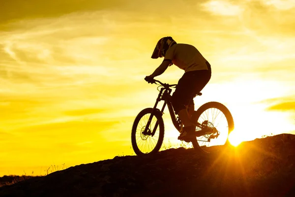 Silhouette of Cyclist Riding Down the Mountain Bike on the Rocky Hill at Sunset. Extreme Sport Concept.