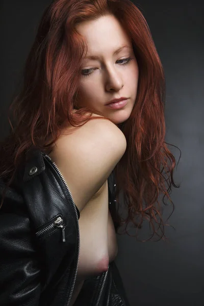 Pretty redhead young woman portrait with leather jacket pulled over shoulder exposing bare breasts.