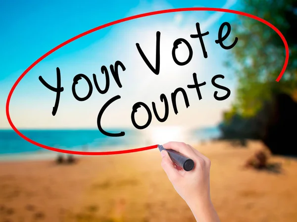 Women Hand writing Your Vote Counts with black marker on visual screen. Isolated on beach. Business, technology, internet concept. Stock Image