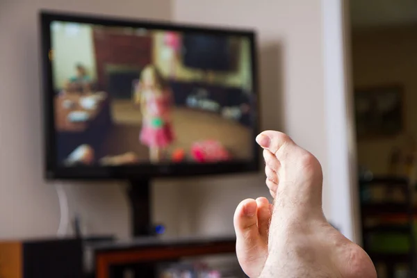 バックグラウンドでテレビで家族の映画を見ている男の焦点で足を持つフィールドの浅い深さ — ストック写真