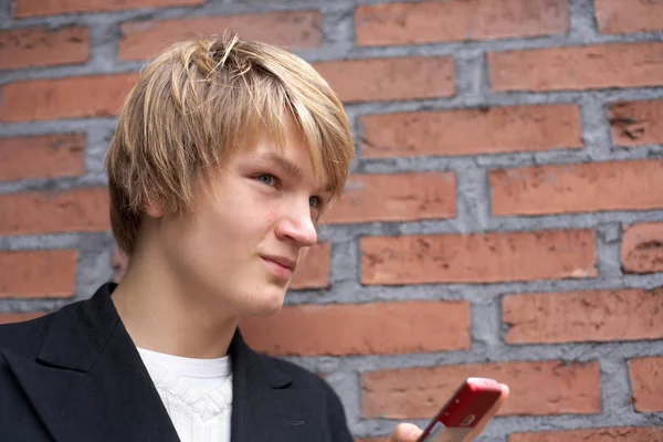 Teenage boy with mobile phone by brick wall, low angle
