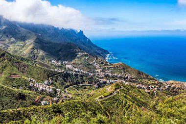 Small city or village and winding or serpantine road in green mountain or rock valley and clouds with horizon landscape near  coast of Atlantic ocean in Tenerife Canary island, Spain clipart