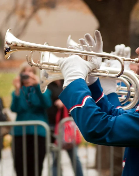 Trumpet played by marching band in parade with woman taking picture in background.
