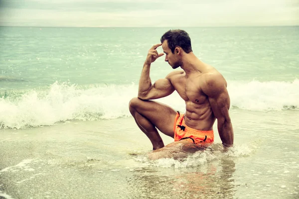在海中配置文件的姿势坐在海滩上肌肉帅哥 — 图库照片