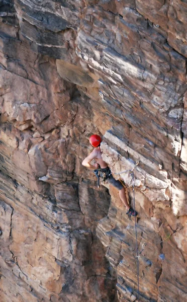 A rock climber works his way up a rock face protected by a rope clipped into bolts. He is wearing a helmet and quickdraws dangle from his harness. The route is in the desert southwest United States. Mt Lemmon, Arizona.