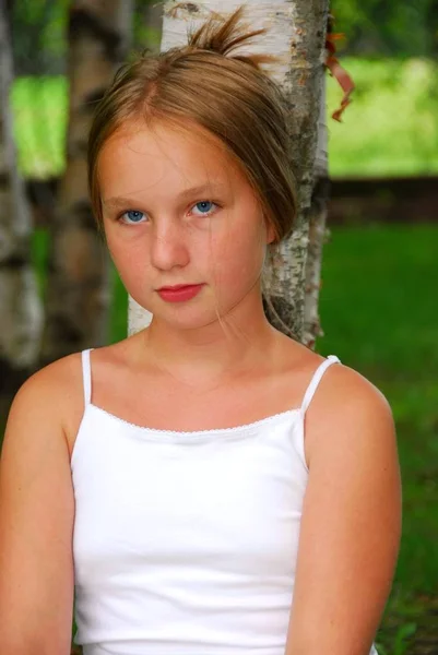 一个年轻的漂亮女孩坐在公园里一棵白杨树下的肖像 — 图库照片