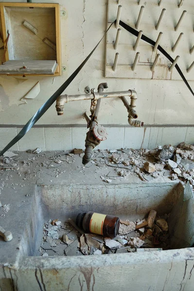 Dirty industrial sink with broken glass bottle of chemical substance and dusty audio reel tape in abandoned vinyl records pressing factory.