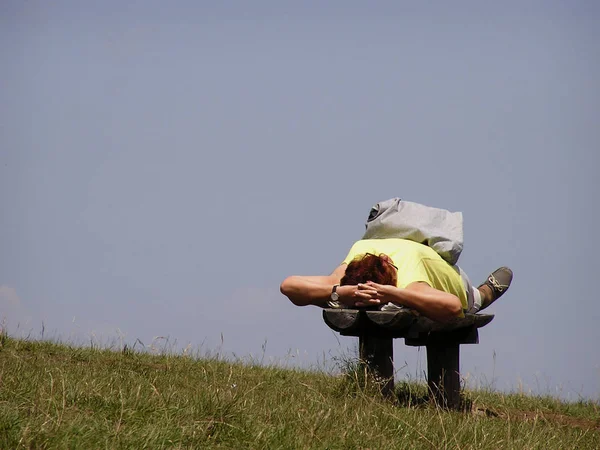 One person resting, sleeping and sunbathing at bench against clear blue sky.