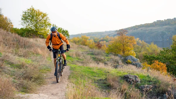 Cyclist in Orange Riding the Mountain Bike on the Autumn Rocky Enduro Trail. Extreme Sport and Enduro Biking Concept.