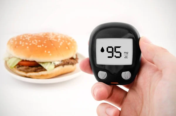 手控股米 糖尿病做血糖水平测试 在背景中的汉堡包 — 图库照片