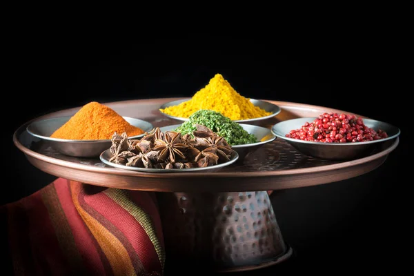 Five colorful spices on a copper presentation plate.