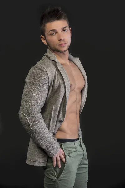 Confident, attractive young man with open jacket on muscular torso, ripped abs and pecs. Side view