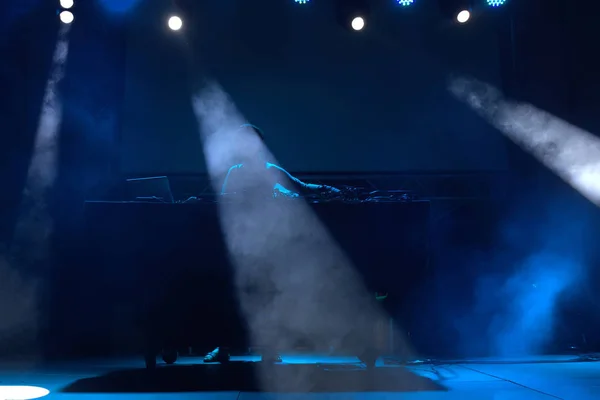 dj performing on a stage with blue lights and smoke.