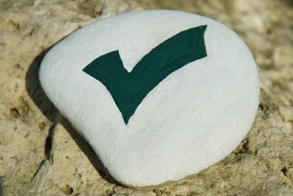 stone with design of green check mark isolated on white over a rock