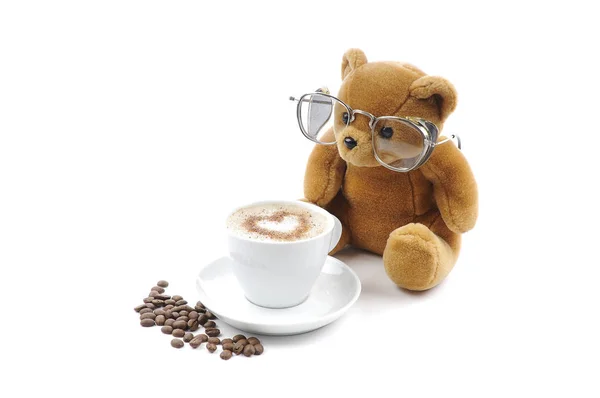 A cup of coffee with foam, shaped into a heart, coffee beans and a Brown Teddy bear, isolated against a white background