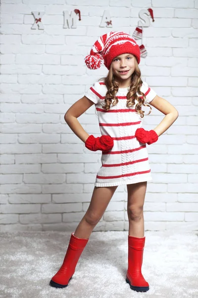 Little fashion girl in fashion Christmas clothes posing over white brick background, full length