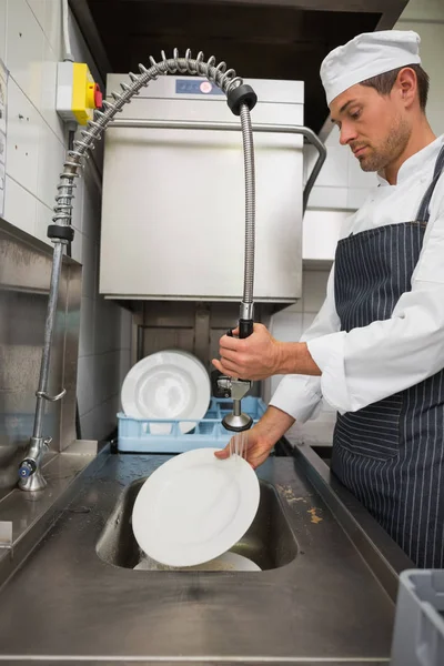Kitchen porter cleaning plates in sink in a commercial kitchen