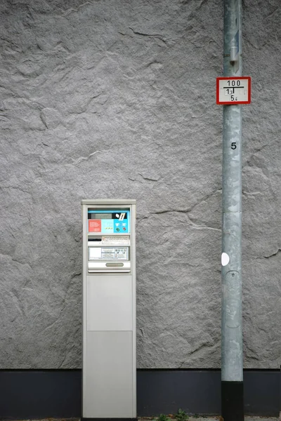An old ticket machine or parking meter is facing a striking wall.
