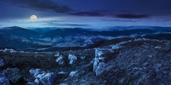 mountain panorama landscape. valley with stones in grass on top of the hillside of mountain range at night in full moon light