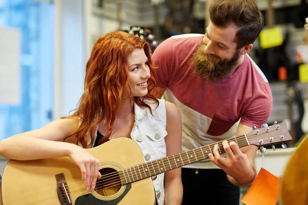 music, sale, people, musical instruments and entertainment concept - happy couple of musicians with guitar at music store