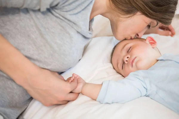 Mother kissing sleeping baby son on bed at home in bedroom