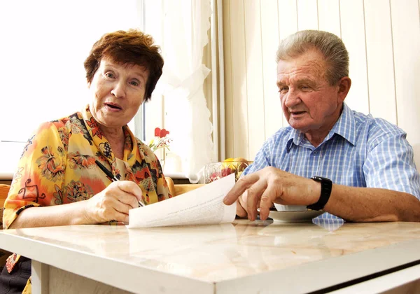 Senior couple signing document in home. Surprised woman