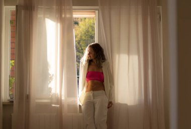 Romantik kız güneş ışıkları evde pencereyakınında beyaz bez güneşin tadını çıkarıyor