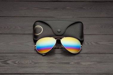 Altın mat siyah ahşap arka plan veya tablo bir siyah deri vaka altın bir daire ve bir deri üzerinde bir yazıt ile bir klip raptiye ile tozunu havacılar güneş gözlüğü cam altın metal çerçeve içinde yapılan yansıtılmış renkli lensler ile kaplı