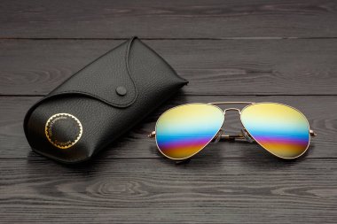 Altın mat siyah ahşap arka plan veya tablo bir siyah deri vaka altın bir daire ve bir deri üzerinde bir yazıt ile bir klip raptiye ile tozunu havacılar güneş gözlüğü cam altın metal çerçeve içinde yapılan yansıtılmış renkli lensler ile kaplı