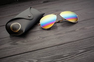 Altın mat siyah ahşap arka plan veya tablo bir siyah deri vaka altın bir daire ve bir deri üzerinde bir yazıt ile bir klip raptiye ile tozunu havacılar güneş gözlüğü cam altın metal çerçeve içinde yapılan yansıtılmış renkli lensler ile kaplı