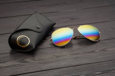 Altın mat siyah ahşap arka plan veya tablo bir siyah deri vaka altın bir daire ve bir deri üzerinde bir yazıt ile bir klip raptiye ile tozunu havacılar güneş gözlüğü cam altın metal çerçeve içinde yapılan yansıtılmış renkli lensler ile kaplı