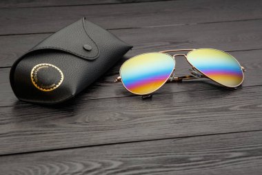 Altın mat siyah ahşap arka plan veya tablo bir siyah deri vaka altın bir daire ve bir deri üzerinde bir yazıt ile bir klip raptiye ile tozunu havacılar güneş gözlüğü cam altın metal çerçeve içinde yapılan yansıtılmış renkli lensler ile kaplı