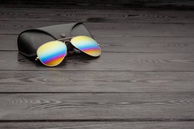 Altın mat siyah ahşap arka plan veya tablo bir siyah deri vaka altın bir daire ve bir deri üzerinde bir yazıt ile bir klip raptiye ile tozunu havacılar güneş gözlüğü cam altın metal çerçeve içinde yapılan yansıtılmış renkli lensler ile kaplı