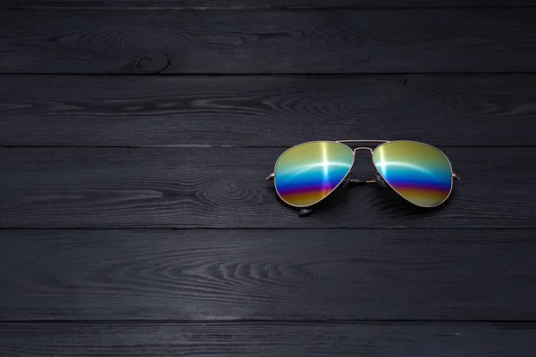 aviators sunglasses with mirrored color lenses made of glass in a gold metal frame and covered with a gold matte finish on a black wooden background or table