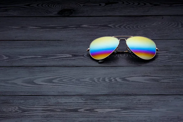 aviators sunglasses with mirrored color lenses made of glass in a gold metal frame and covered with a gold matte finish on a black wooden background or table