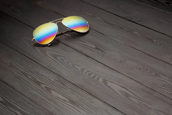 aviators sunglasses with mirrored color lenses made of glass in a gold metal frame and covered with a gold matte finish on a black wooden background or table