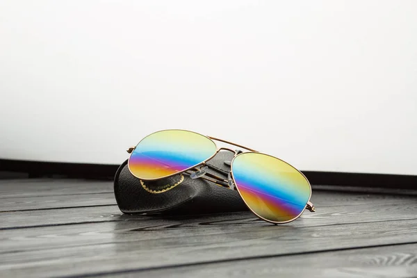 aviators sunglasses with mirrored color lenses made of glass in a gold metal frame covered with gold matte dusting on a black wooden background or table with a black leather case with a clip fastener with a gold circle and an inscription on a leather