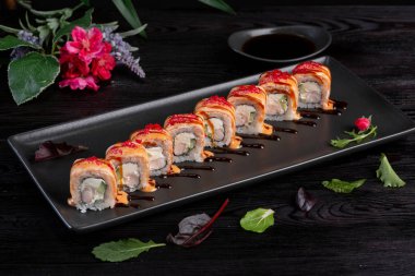 Koyu ahşap arka plan üzerinde siyah bir dikdörtgen plaka üzerinde set suşi rulo