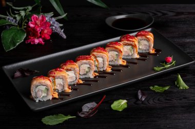 Koyu ahşap arka plan üzerinde siyah bir dikdörtgen plaka üzerinde set suşi rulo