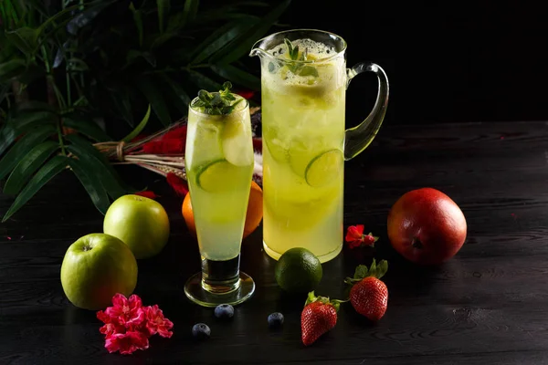 Bir sürahi ve cam ve koyu ahşap arka plan üzerinde meyve kireç ile yeşil elma limonata